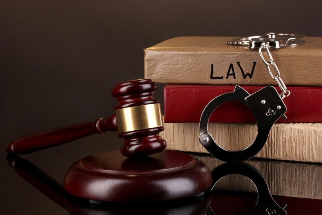 A gavel, handcuffs, and law books are isolated against a black background.