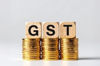Three gray cubes labeled "GST Concept" are stacked on a surface with several golden coins scattered around them.