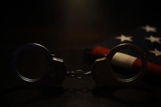 Handcuffs rest on top of an American flag, lit in a dark setting, suggesting law enforcement and justice.