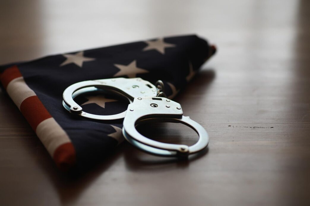 Handcuffs rest on a folded American flag, symbolizing justice, law enforcement, and patriotism.