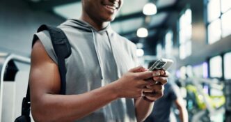 A man in a gym uses a smartphone, likely tracking fitness progress or using a health app.