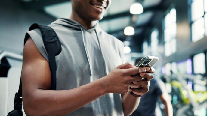 A man in a gym uses a smartphone, likely tracking fitness progress or using a health app.