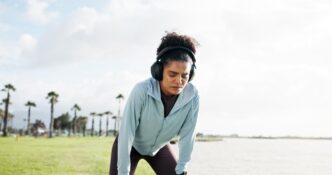 A woman wearing headphones rests on the edge of a lake, appearing exhausted after a workout.