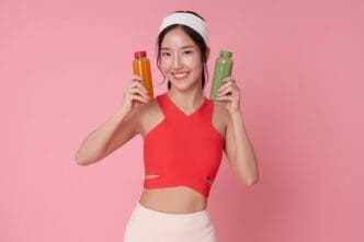 Asian woman in fitness attire holding bottles of detox juice, promoting wellness.