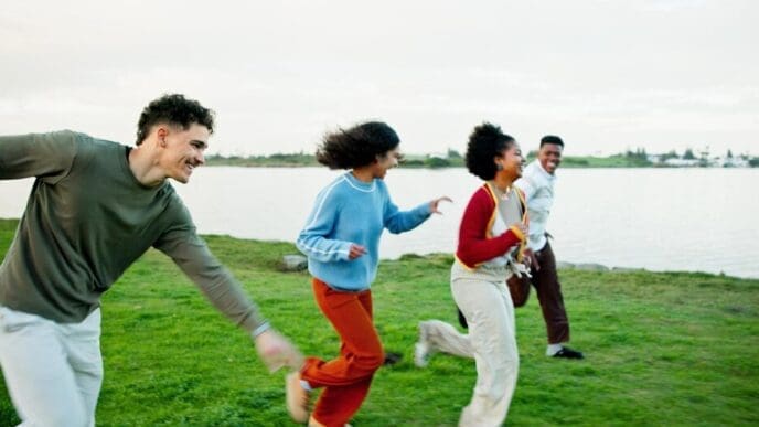 A group of diverse friends races outdoors near a lake, appearing happy and energetic during a vacation or gap year.