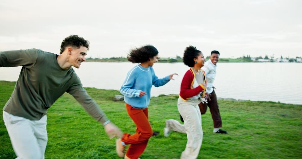 A group of diverse friends races outdoors near a lake, appearing happy and energetic during a vacation or gap year.