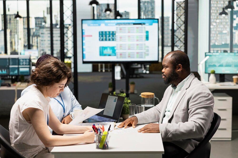 Two HR staff members interview a job seeker in a modern corporate office setting.