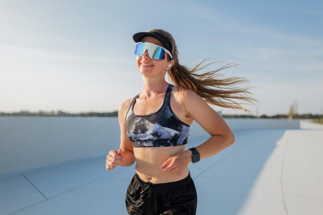 A runner in athletic wear smiles while enjoying a sunny day.