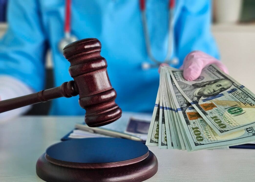 A judge holds a gavel while a medical professional presents stacks of cash in a courtroom setting.