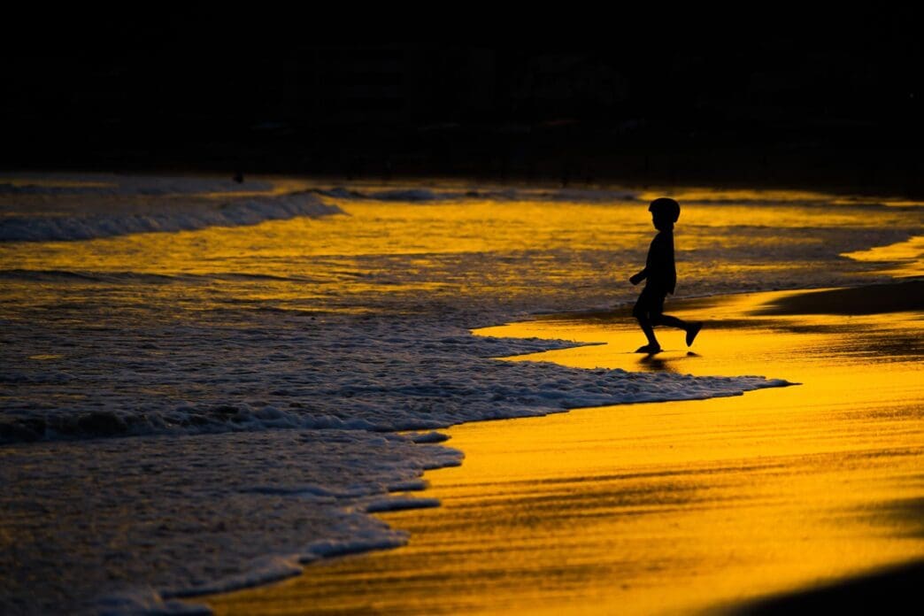 A child plays in the waves at dusk.