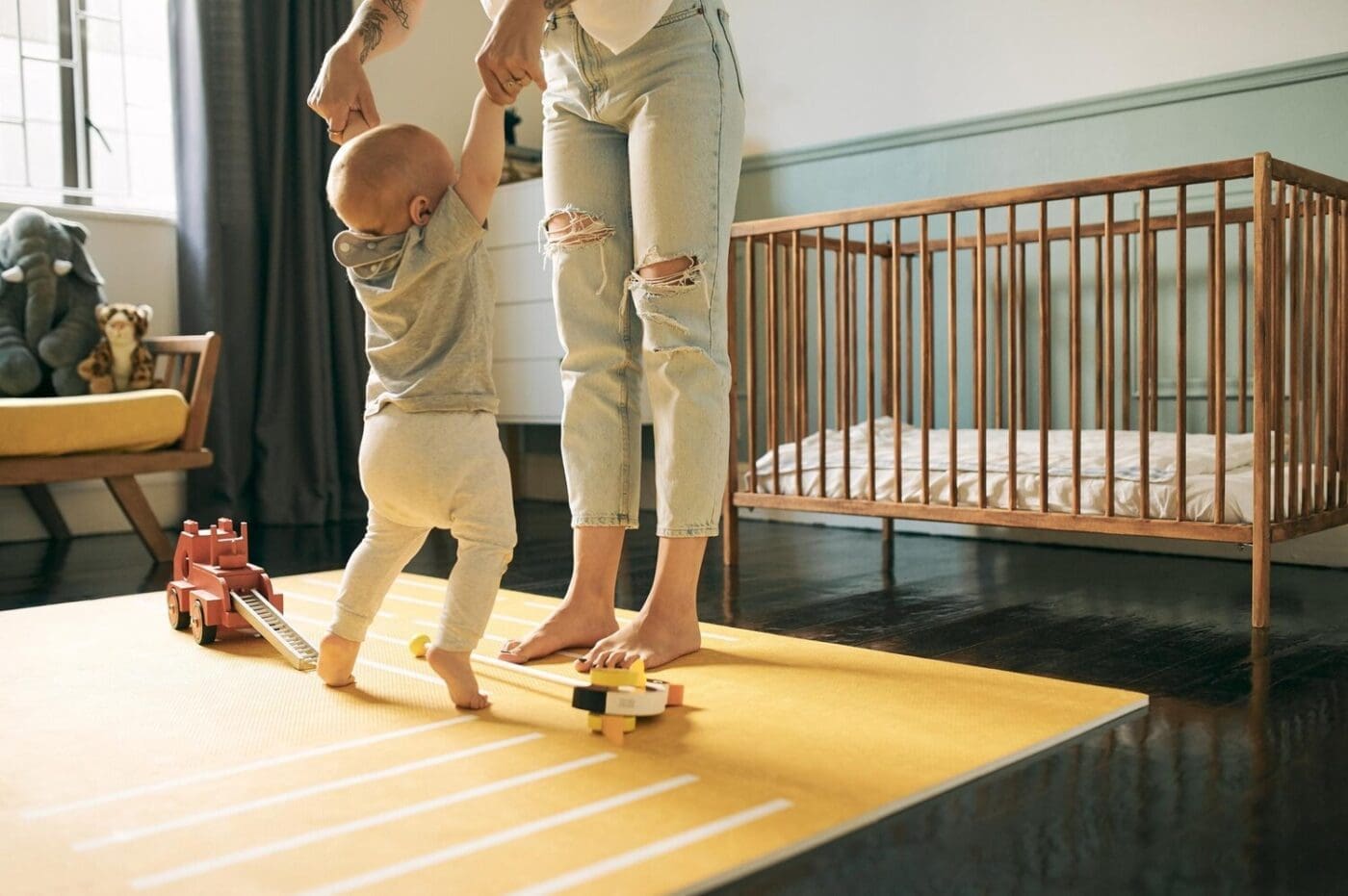 A mother and baby dance and enjoy quality time together in a nursery, with the child learning to walk with support.