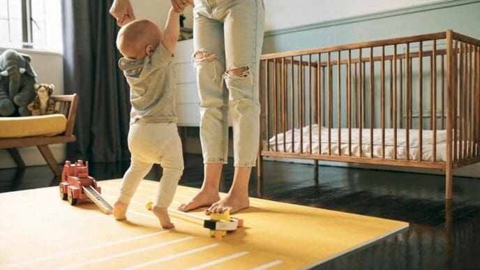 A mother and baby dance and enjoy quality time together in a nursery, with the child learning to walk with support.