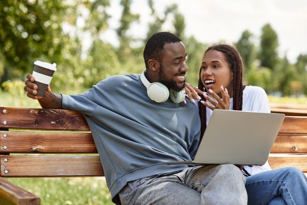 A smiling couple sits close together on a park bench, enjoying a sunny afternoon.
