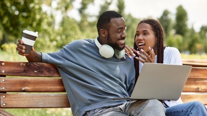 A smiling couple sits close together on a park bench, enjoying a sunny afternoon.