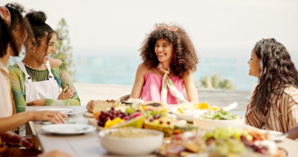 Group of women laughing and enjoying food and conversation at an outdoor party or social gathering.