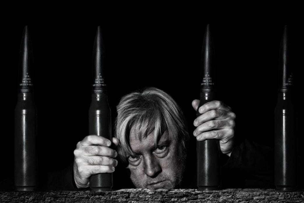 A man poses for a selfie behind bars formed by stacked ammunition cartridges.