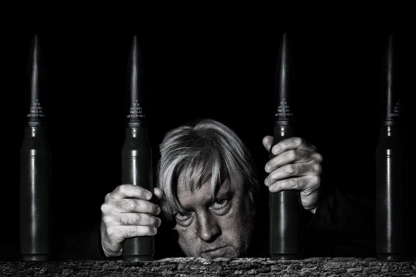 A man poses for a selfie behind bars formed by stacked ammunition cartridges.