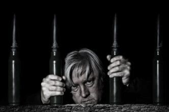 A man poses for a selfie behind bars formed by stacked ammunition cartridges.