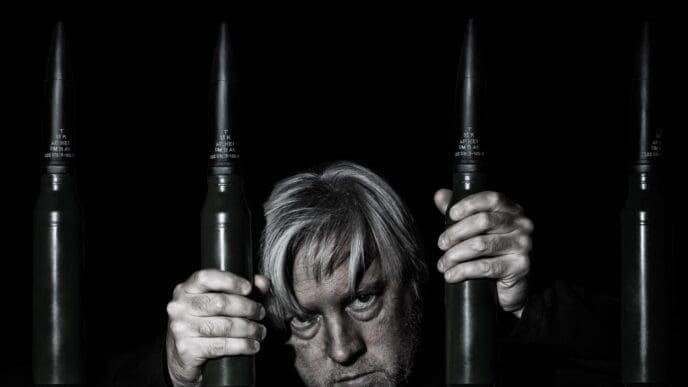 A man poses for a selfie behind bars formed by stacked ammunition cartridges.