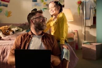 A middle-aged man smiles while playing with a young girl inside.