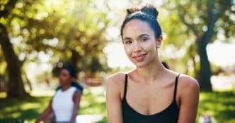 A smiling woman in a portrait poses outdoors, representing a yoga instructor promoting holistic healing and mindfulness.