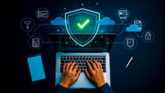 Person typing on a laptop with a digital shield and data icons superimposed, representing cybersecurity and protection.