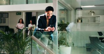 A businessperson smiles while reading a phone in an office setting.