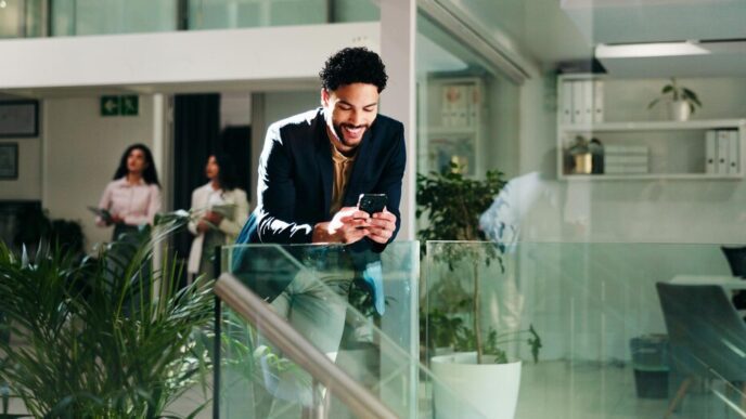 A businessperson smiles while reading a phone in an office setting.
