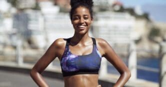 A smiling Black woman in sportswear takes a break during an outdoor running routine in the city.