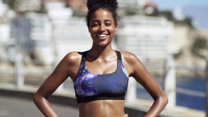 A smiling Black woman in sportswear takes a break during an outdoor running routine in the city.