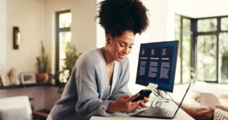 A woman works remotely on a phone and computer in a home office, likely for a consulting business, startup, or project management.