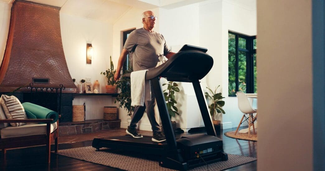 An elderly man walks on a treadmill in a home gym setting, engaging in a cardio workout for fitness.