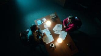 Two professionals converse intently in a dimly lit office at night.