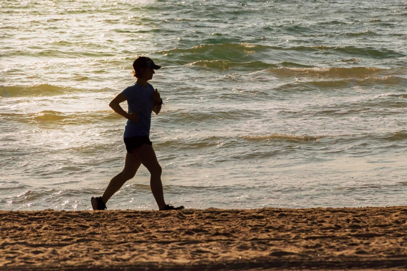 Silhouette of a person running on the beach at dawn, with the sun rising over the water at Malvarrosa beach in Valencia, Spain.