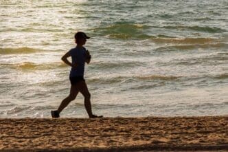 Silhouette of a person running on the beach at dawn, with the sun rising over the water at Malvarrosa beach in Valencia, Spain.