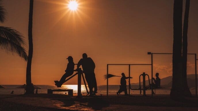 Silhouettes of elderly Vietnamese people exercise on horizontal bars at a sports ground by the sea at sunrise.