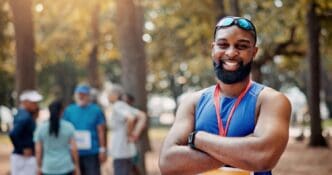 A smiling marathon runner with arms crossed confidently poses for a portrait, embodying wellness and fitness.