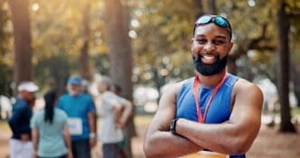 A smiling marathon runner with arms crossed confidently poses for a portrait, embodying wellness and fitness.