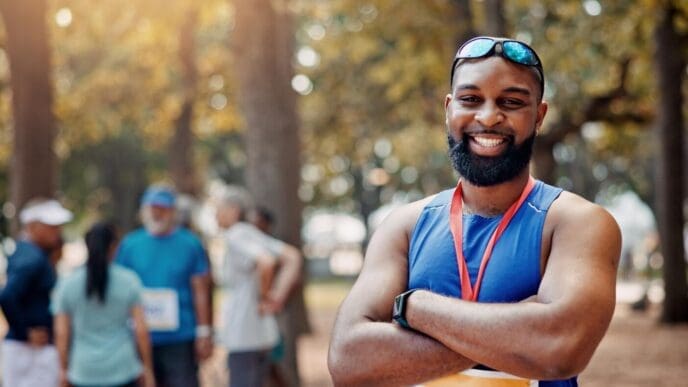A smiling marathon runner with arms crossed confidently poses for a portrait, embodying wellness and fitness.
