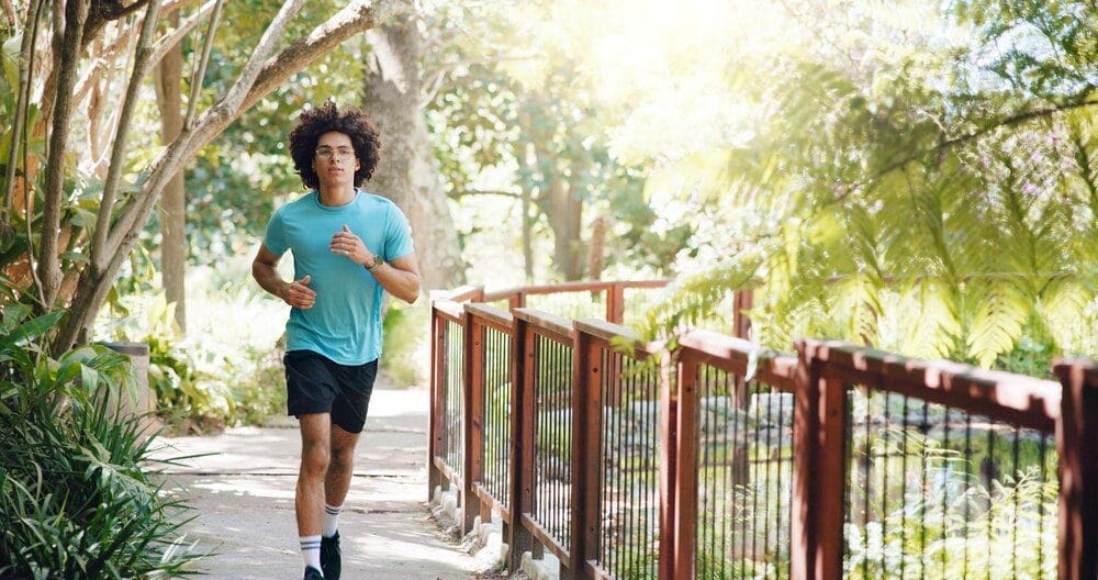 A man runs on a path in a park, engaging in cardio exercise for fitness and marathon training.