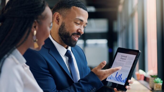 Tablet screen displaying graphs and data during a meeting with people, likely for an annual report or business analysis.