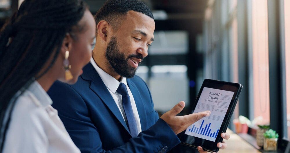 Tablet screen displaying graphs and data during a meeting with people, likely for an annual report or business analysis.