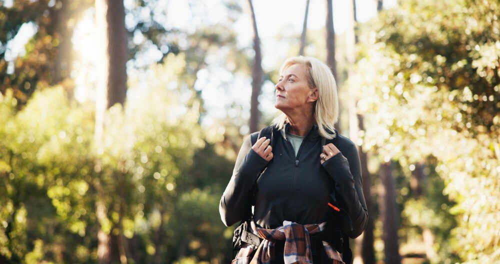 An older woman hikes through a forest.