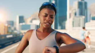 A tired woman in fitness attire checks her watch, possibly after a workout in the city.