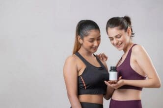 Two women in athletic wear examine a supplement bottle.