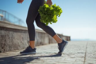A woman jogs outdoors, holding fresh lettuce, representing a healthy lifestyle and fitness.