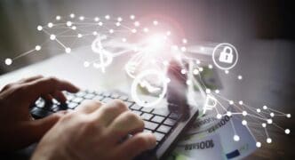 A person works on a laptop and keyboard with 100 euro bills scattered on the table.