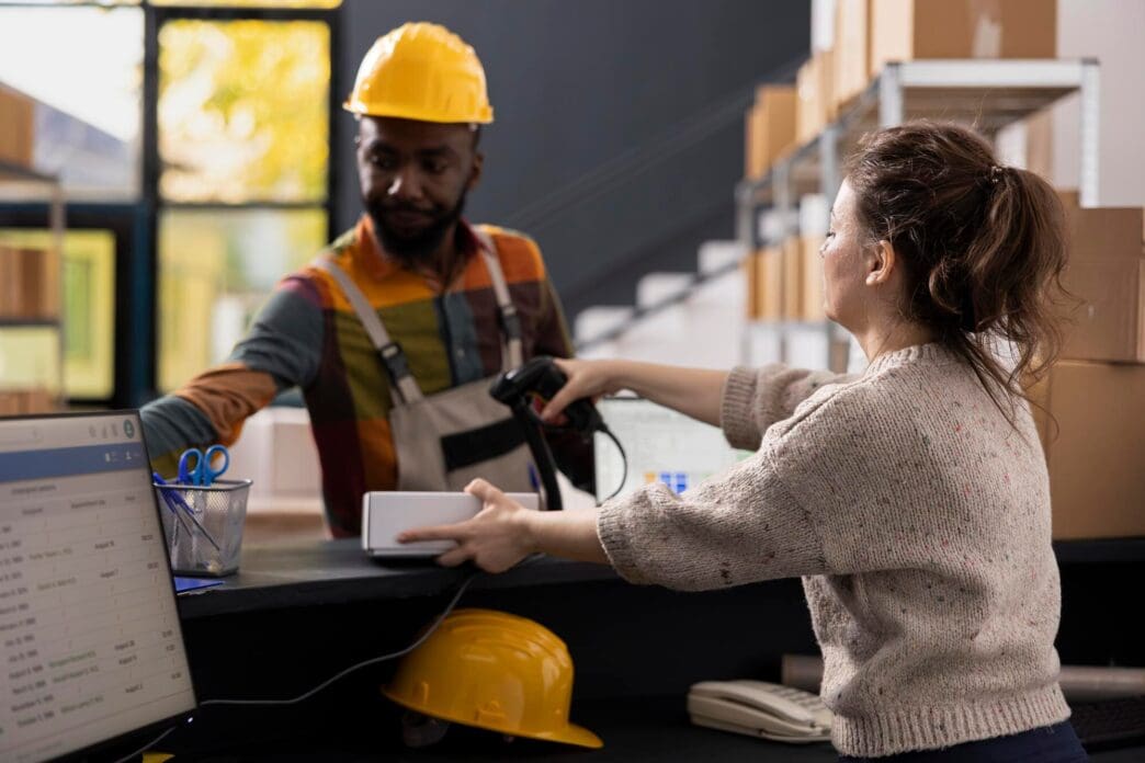 Workers in a storage facility scan barcodes on boxes with handheld scanners.