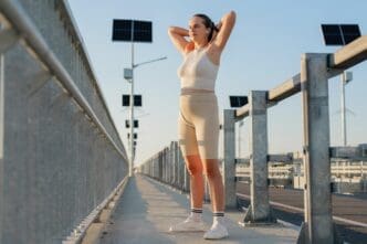 A young woman in athletic wear stretches on a sunny bridge, with solar panels visible in the background.