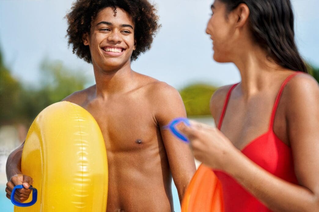 Young adults enjoy themselves in a swimming pool, some using inflatable floats.